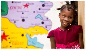 A young girl stands next to a map in her classroom in Haiti